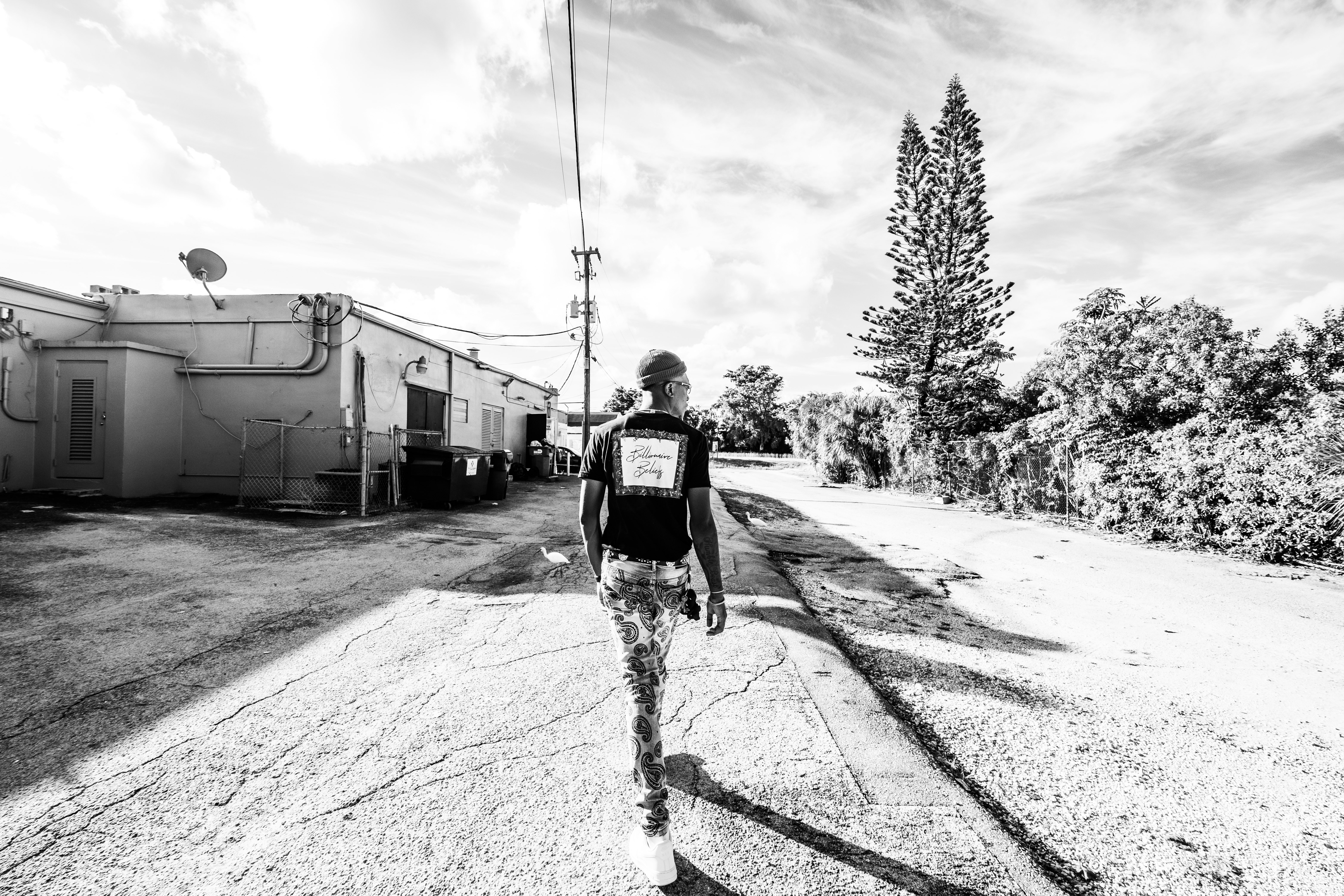 grayscale photo of man in black jacket and pants walking on road